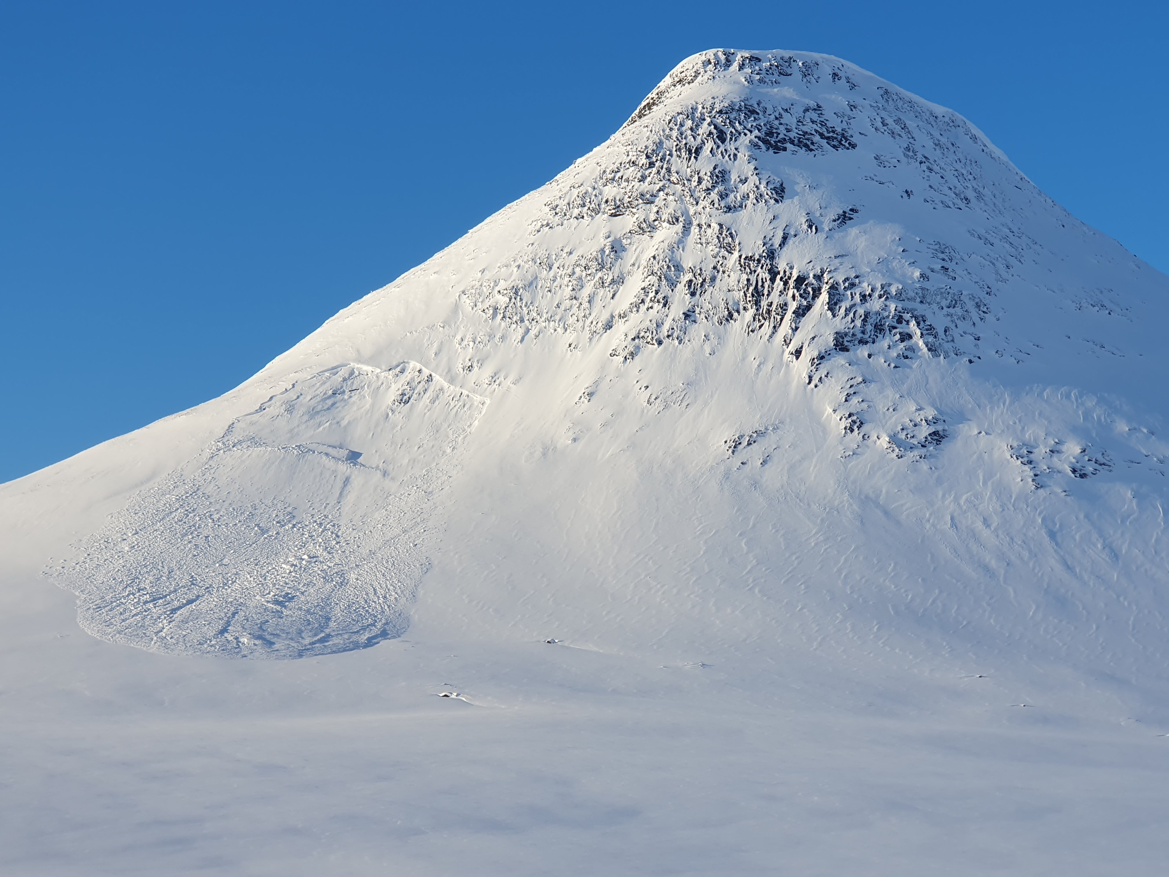 Snöklätt fjäll där man ser att en lavin utlösts. Blå himmel bakom.